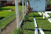 A chain link fence being replaced by a white vinyl fence in a lush green backyard