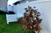 A newly installed white vinyl fence in a lush green backyard